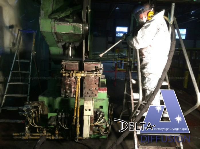 Nettoyage par projection de glace carbonique sur une machine industrielle, opérateur en équipement de protection avançant avec un pistolet cryogénique. Delta Diffusion. yage par projection de glace carbonique